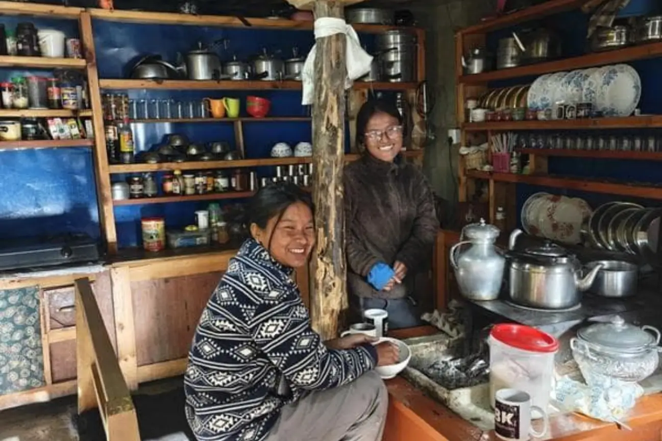 Local teahouse staff smiling inside a rustic kitchen filled with cookware during a Nepal Trekking Annapurna excursion.