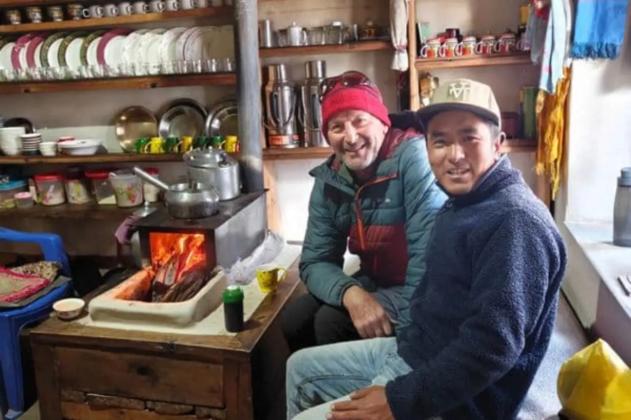 Trekkers warming up by a traditional wood-burning stove inside a cozy mountain teahouse during a Nepal Trekking Annapurna trip.