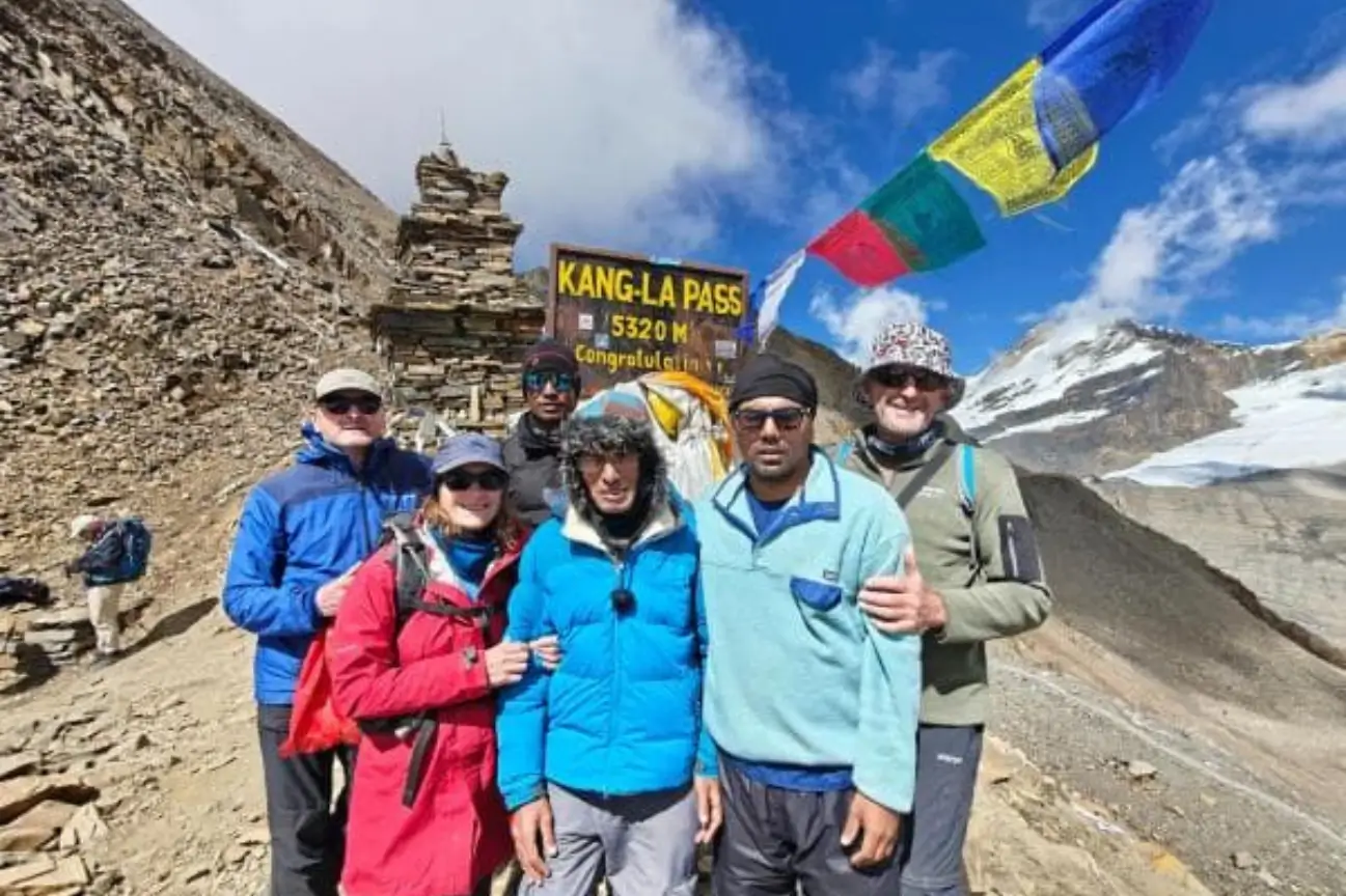 Conquer Group Treks On Nepal Trekking Annapurna A diverse group of smiling trekkers and guides posing at the Kang La Pass sign during a Nepal Trekking Annapurna expedition.
