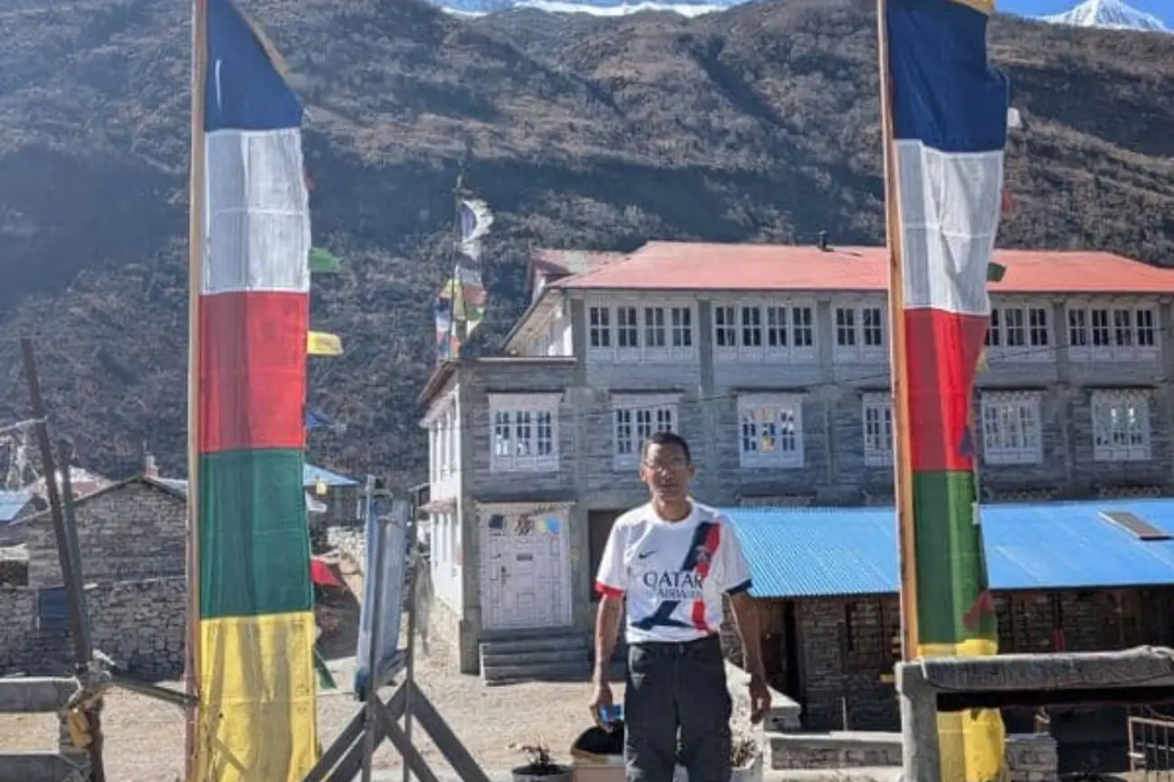 Discover Nature On Nepal Trekking Annapurna A guide standing between large prayer flags with a mountain lodge background during a Nepal Trekking Annapurna trip.