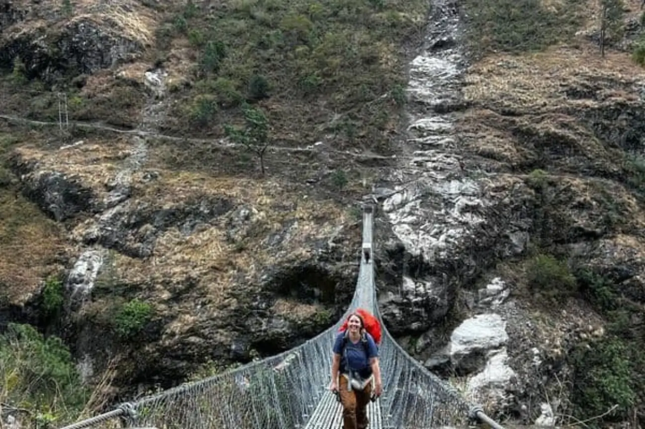 Explore Scenic Lakes And Valleys On Nepal Trekking Annapurna A hiker crossing a long suspension bridge over a deep valley during a Nepal Trekking Annapurna excursion.